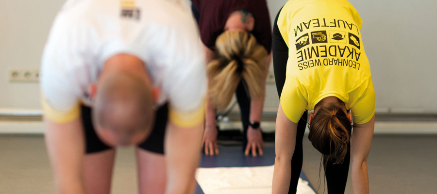 Firmenfitness_Leonhard-Weiss Porträt einer lächelnden Frau mit leuchtend roten Haaren in grünem Sportshirt. Sie trägt eine silberne Kette und steht vor einem hellen, natürlichen Hintergrund. Es handelt sich um Simone Hemming, die Inhaberin der Sportscheune.
