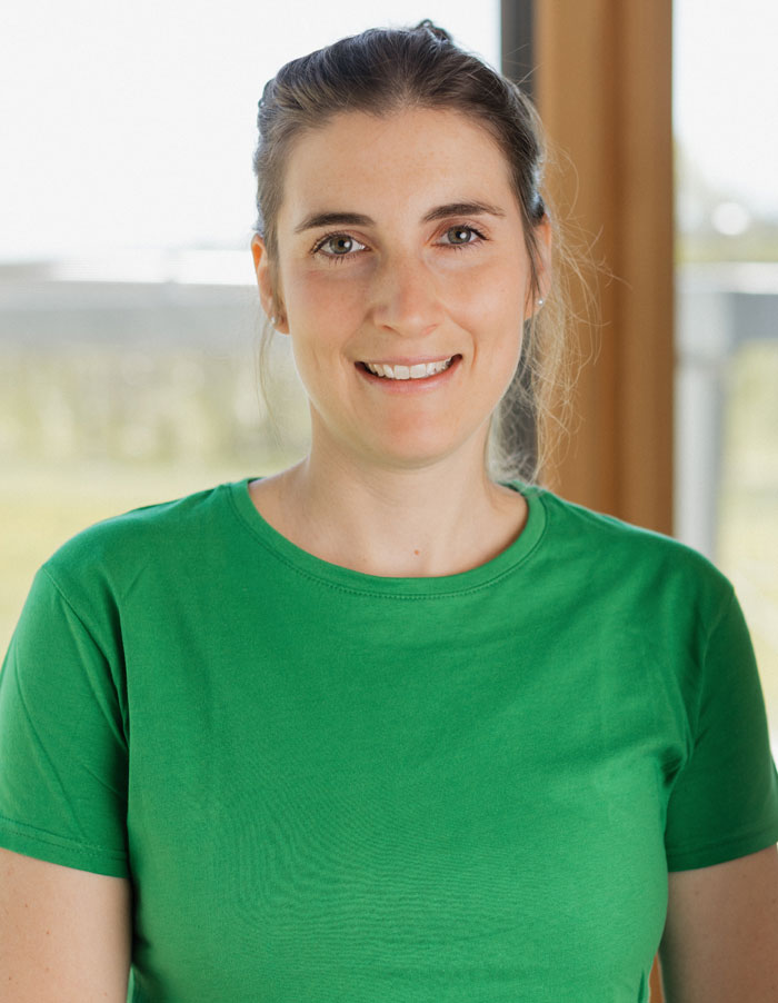 Caroline Team Sportscheune – Empfang & Betreuung - im grünen T-Shirt lächelt vor hellem Hintergrund.